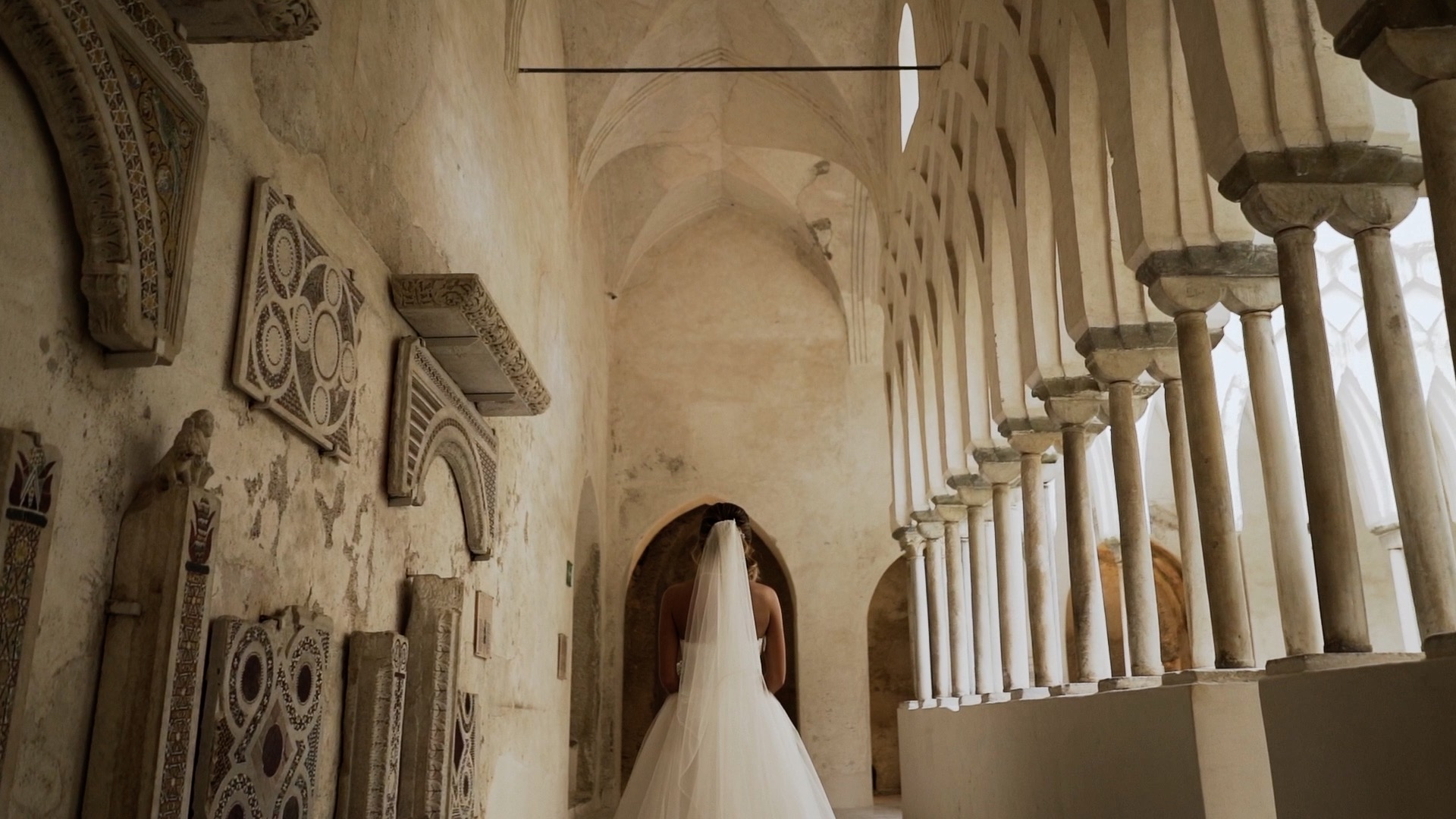 A bride walking through an arched stone cloister