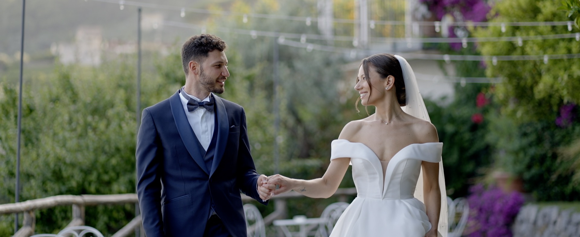 Bride and groom holding hands beside a garden