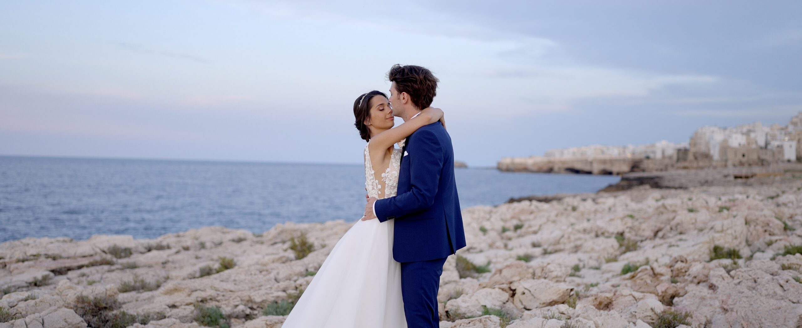 Federica and Riccardo embracing on the coast at Polignano a Mare