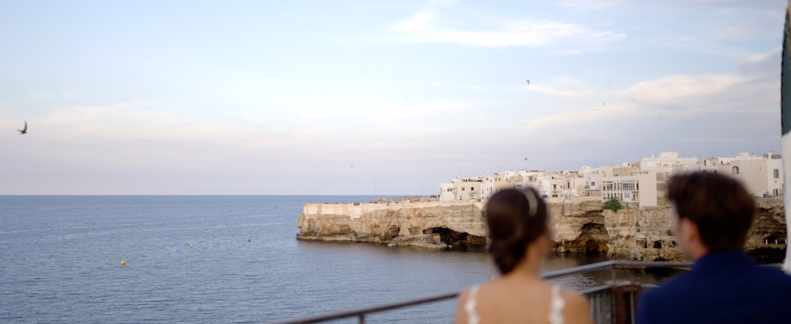 A couple overlooking the sea and waterfront buildings in Polignano a Mare