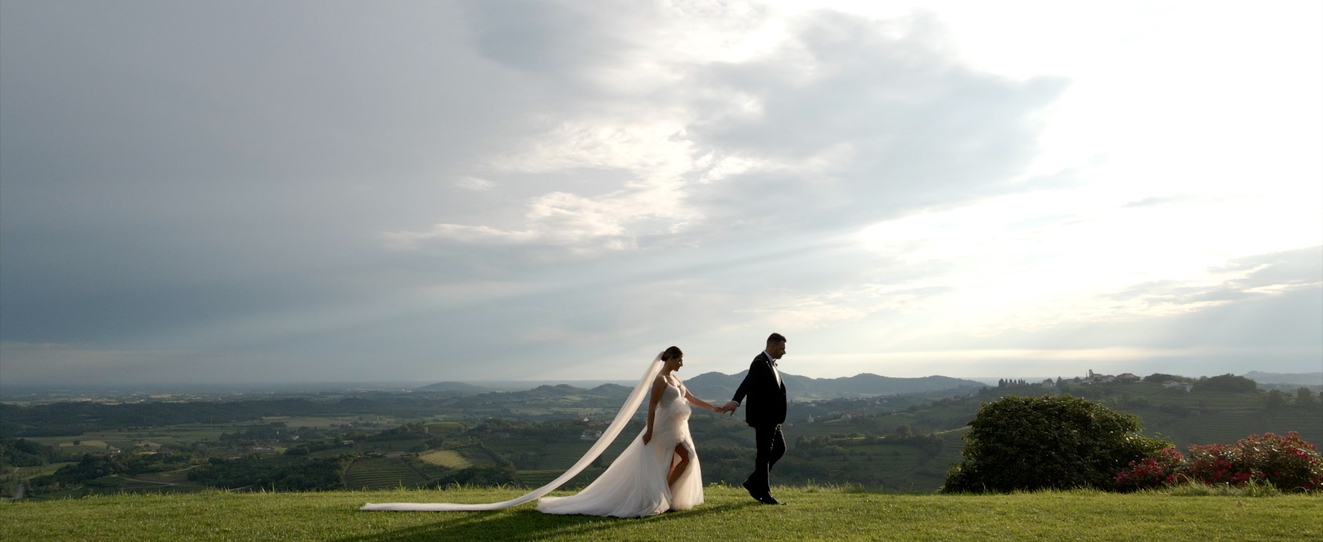 Bride and groom on a grassy hillside beneath a cloudy sky