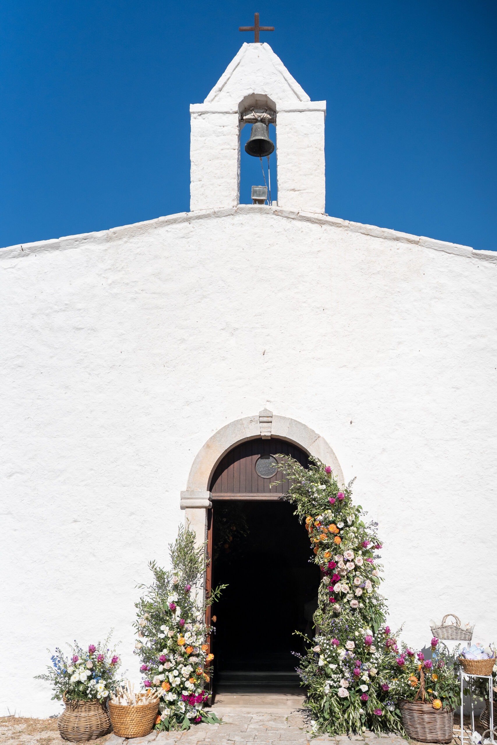 White facade and flower-framed entrance of San Michele in Frangesto church in Monopoli, Puglia.