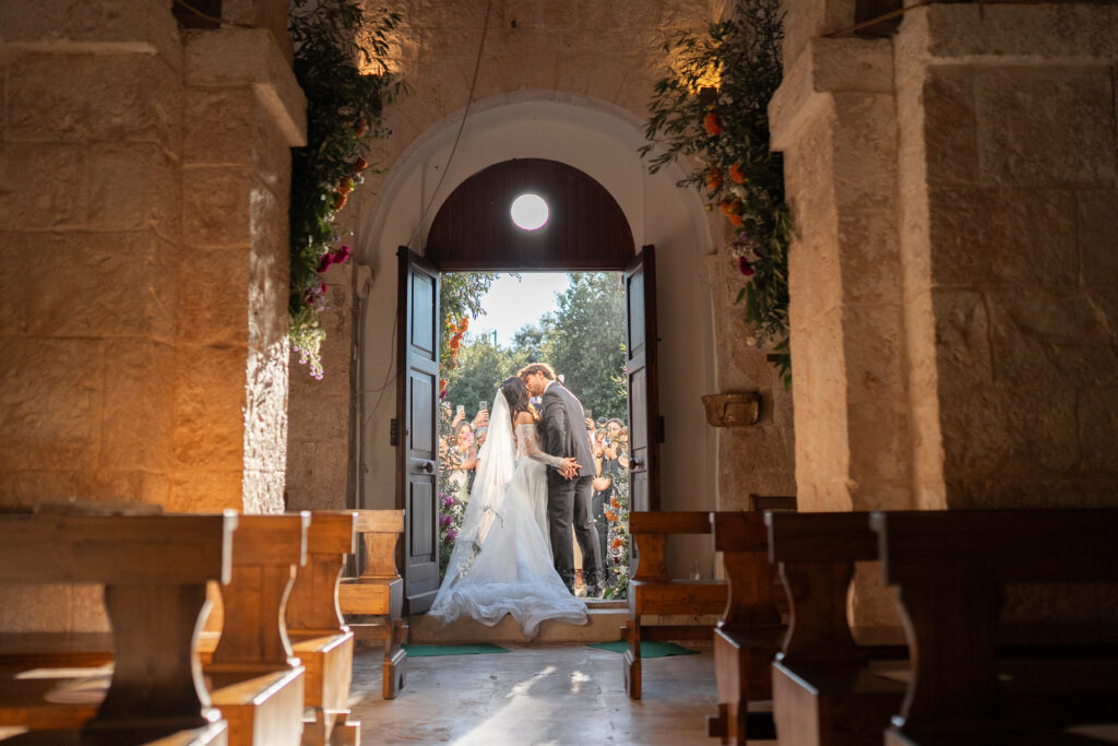 Angel and Andrea kissing among their wedding guests in the warm evening light.