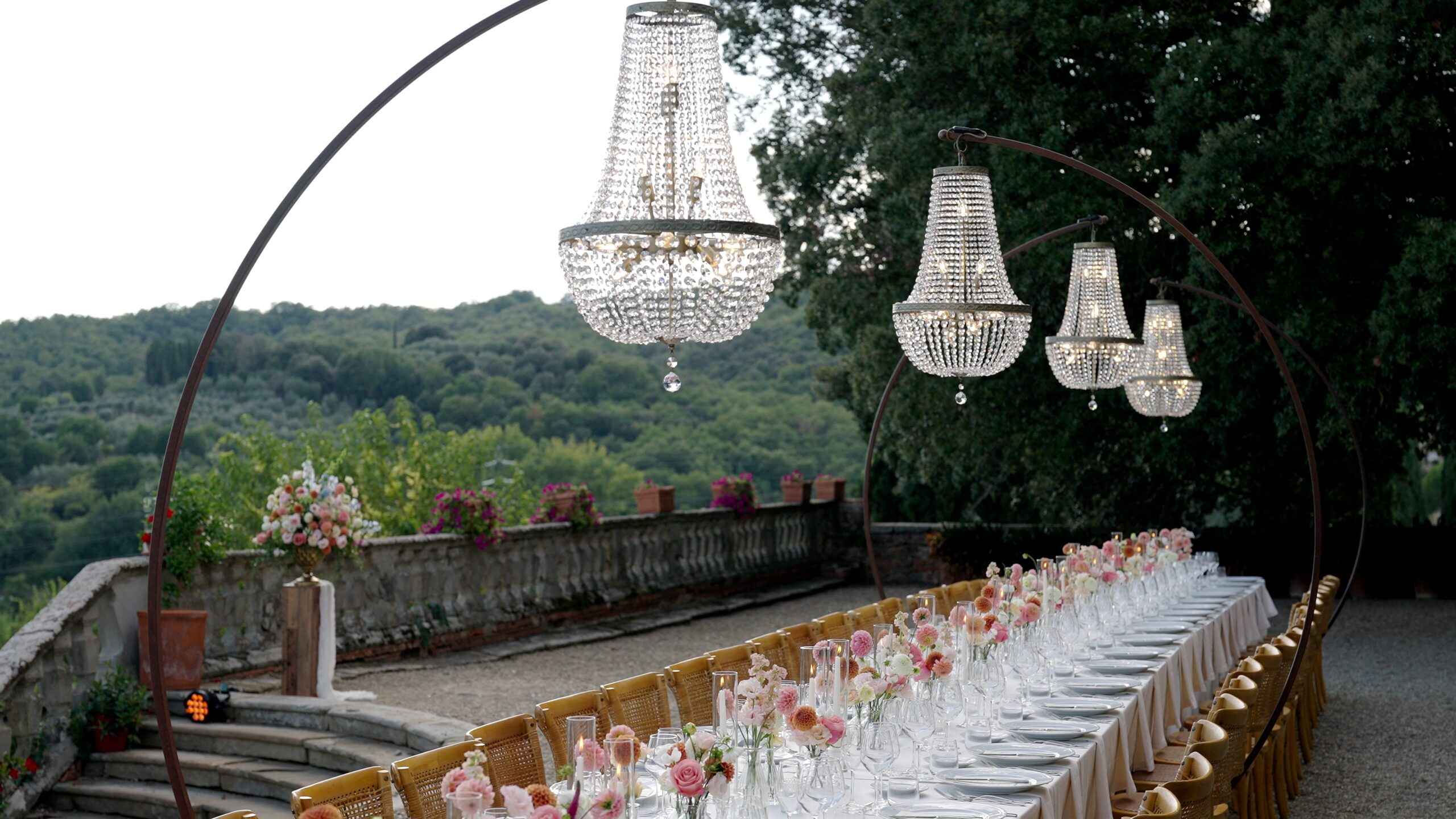 Long outdoor wedding table with pink flowers and chandeliers at Villa Fabbriche Palma in Tuscany.