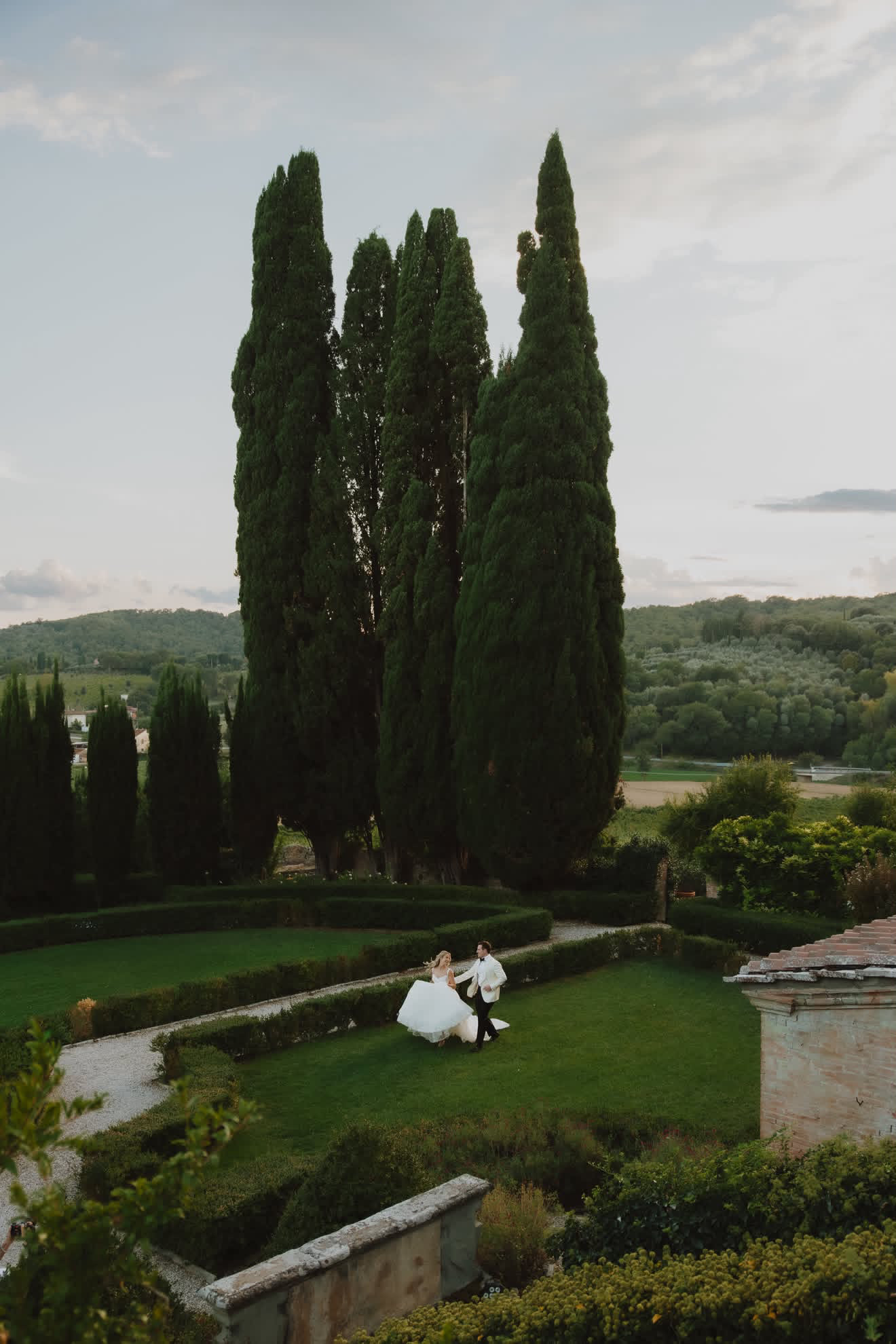 Chloe and Mike walking through the Italian garden beneath the cypress trees at Villa Fabbriche Palma.