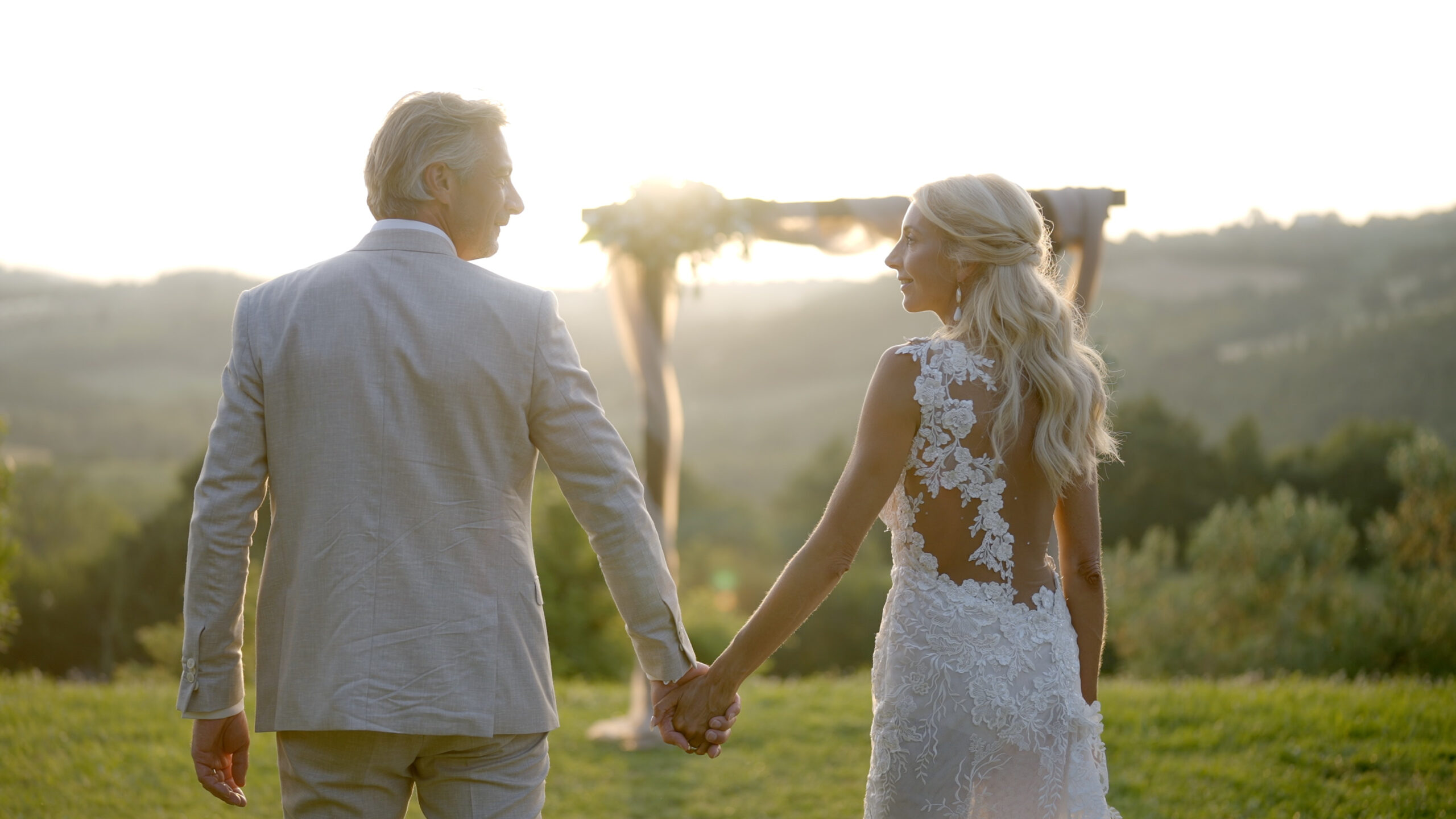 Gerben and Lonneke holding hands in the evening light, with their ceremony arch behind them.