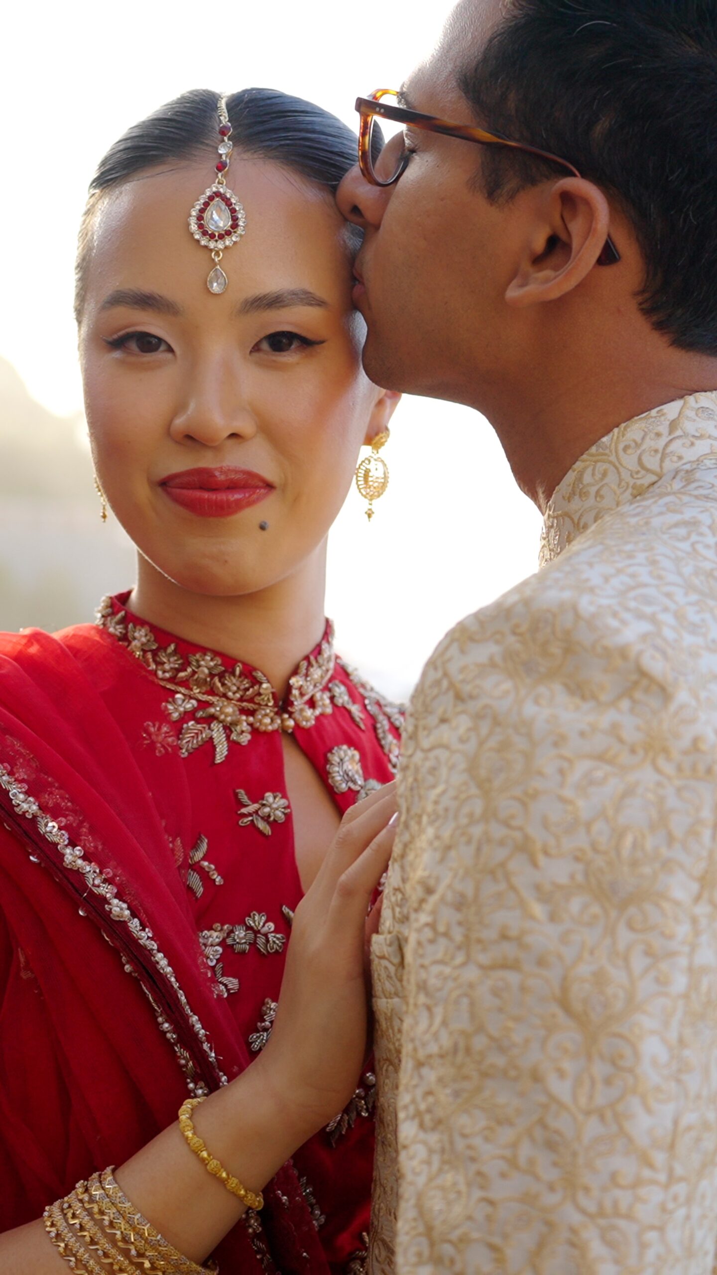 Sheh kissing Gaia&rsquo;s forehead as she wears a red embroidered outfit and bridal jewellery.