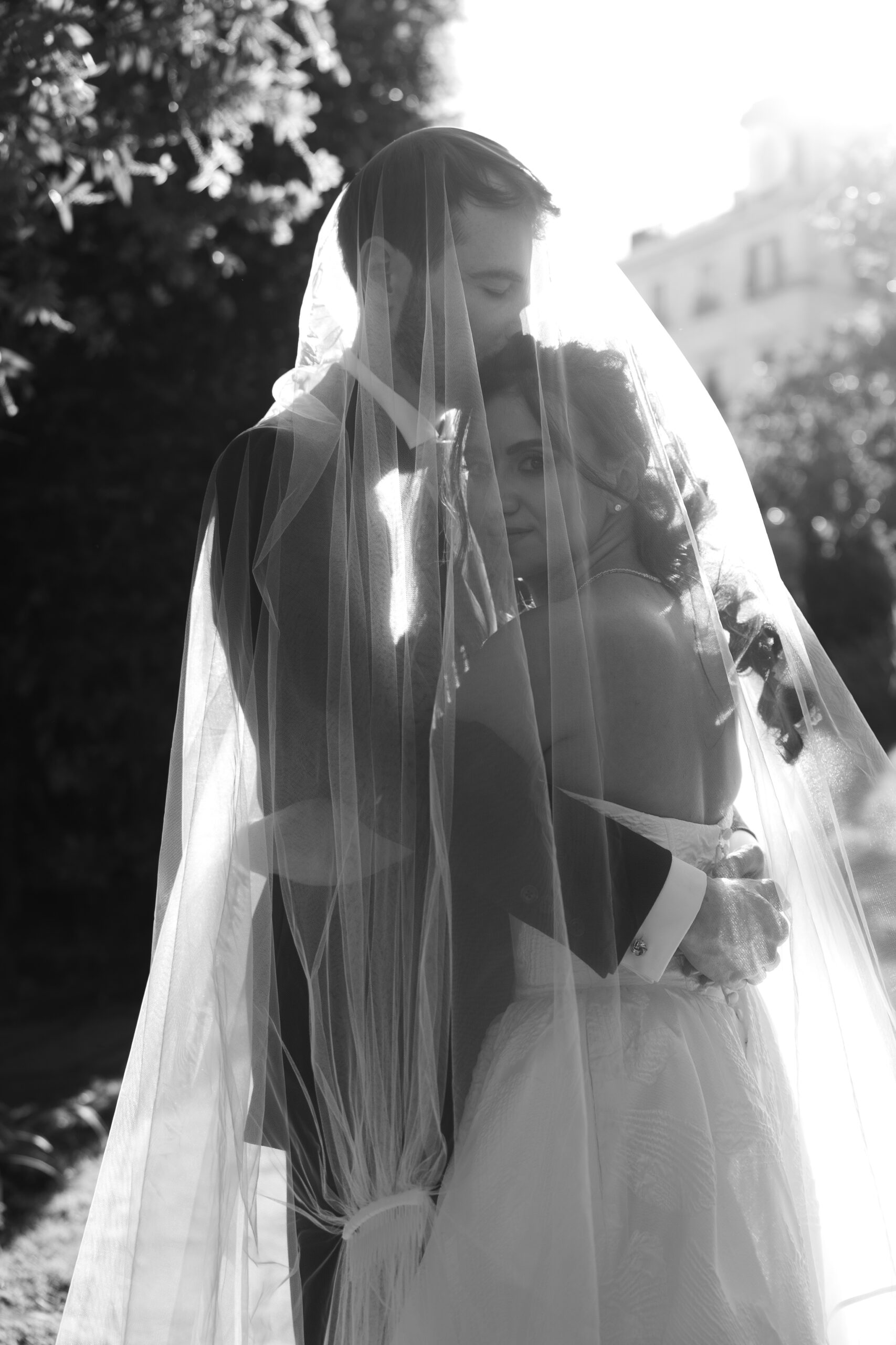 Monica and Jack embracing beneath her veil in a black and white wedding portrait.