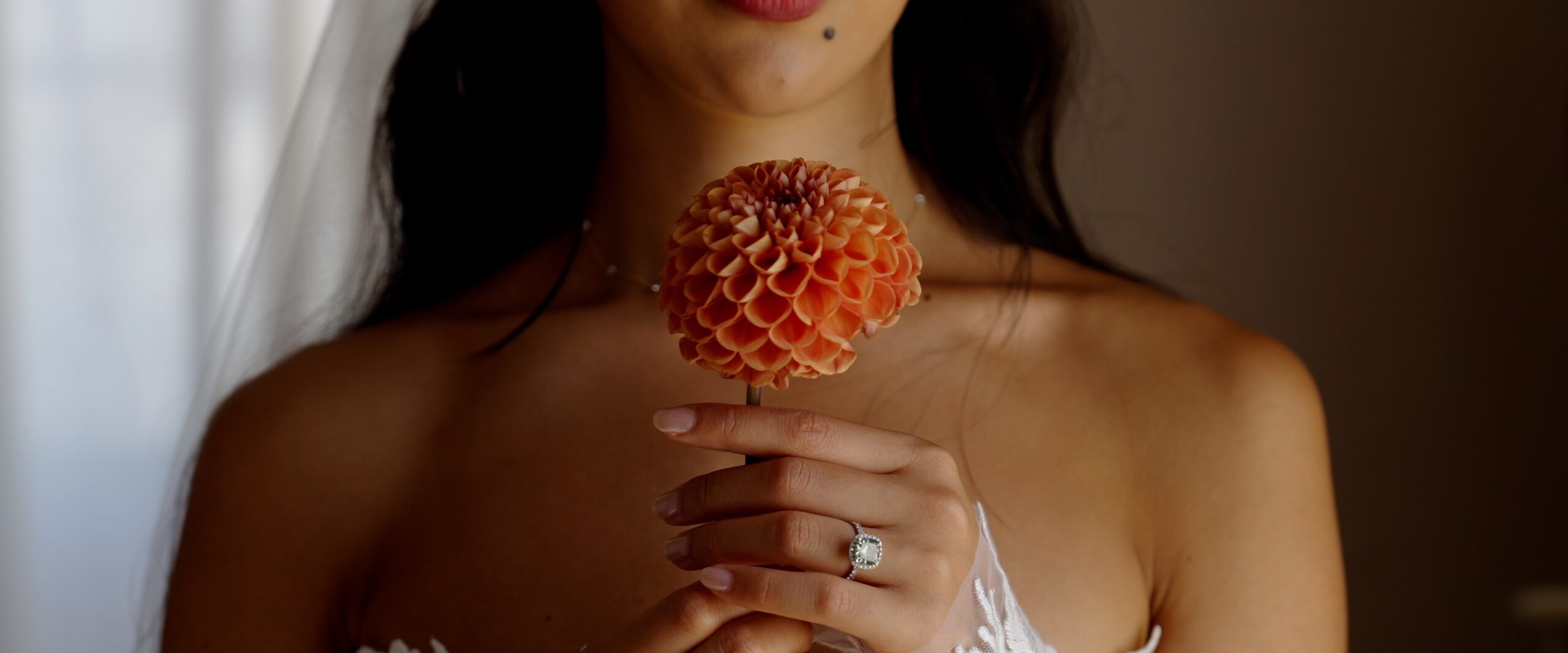 Gaia holding an orange dahlia, with her engagement ring and lace sleeve visible.